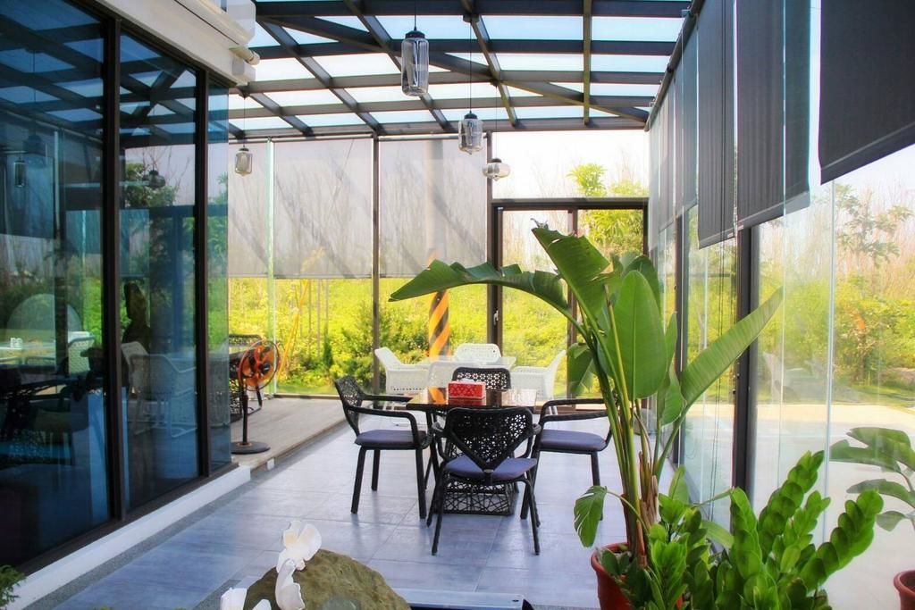 An outdoor patio with a table and chairs, surrounded by glass walls and a view of greenery.