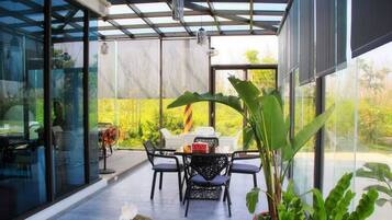 An outdoor patio with a table and chairs, surrounded by glass walls and a view of greenery.