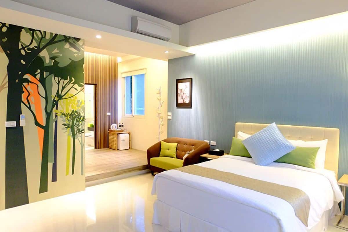 A modern hotel room with a large bed, a seating area, and a view of the hallway.