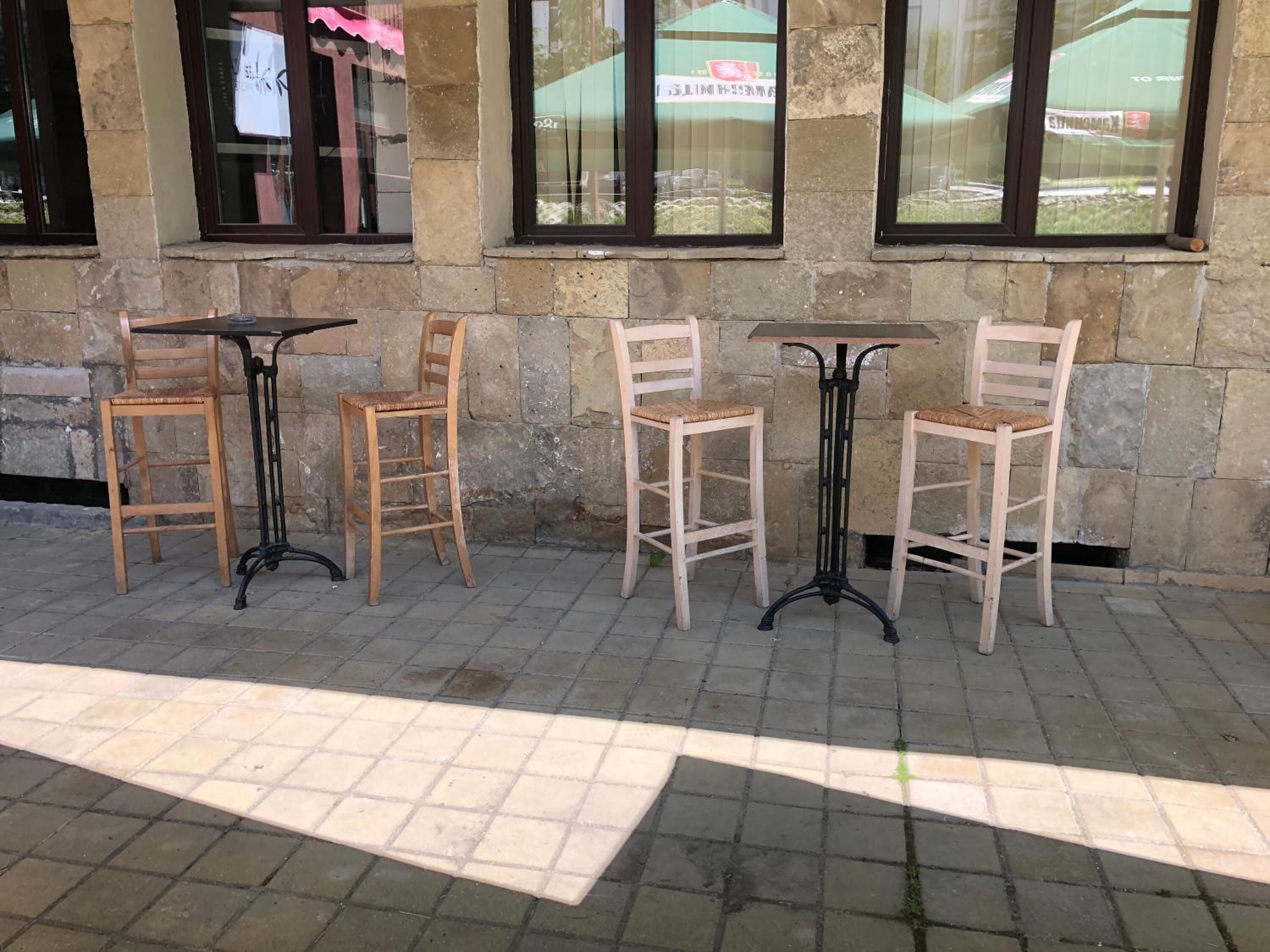 A row of wooden chairs and tables aligned against a stone wall with windows.