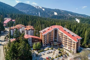 Un hôtel à plusieurs étages, avec un toit rouge, entouré d’une forêt dense et de montagnes.