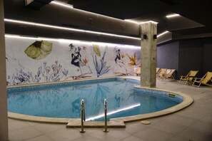 Une piscine intérieure dont le mur est décoré d’une fresque représentant des motifs aquatiques et floraux.