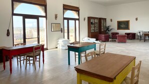 A spacious living room with large windows, a wooden cabinet, a dining table, and several chairs. - Masseria Vico (Nardò)