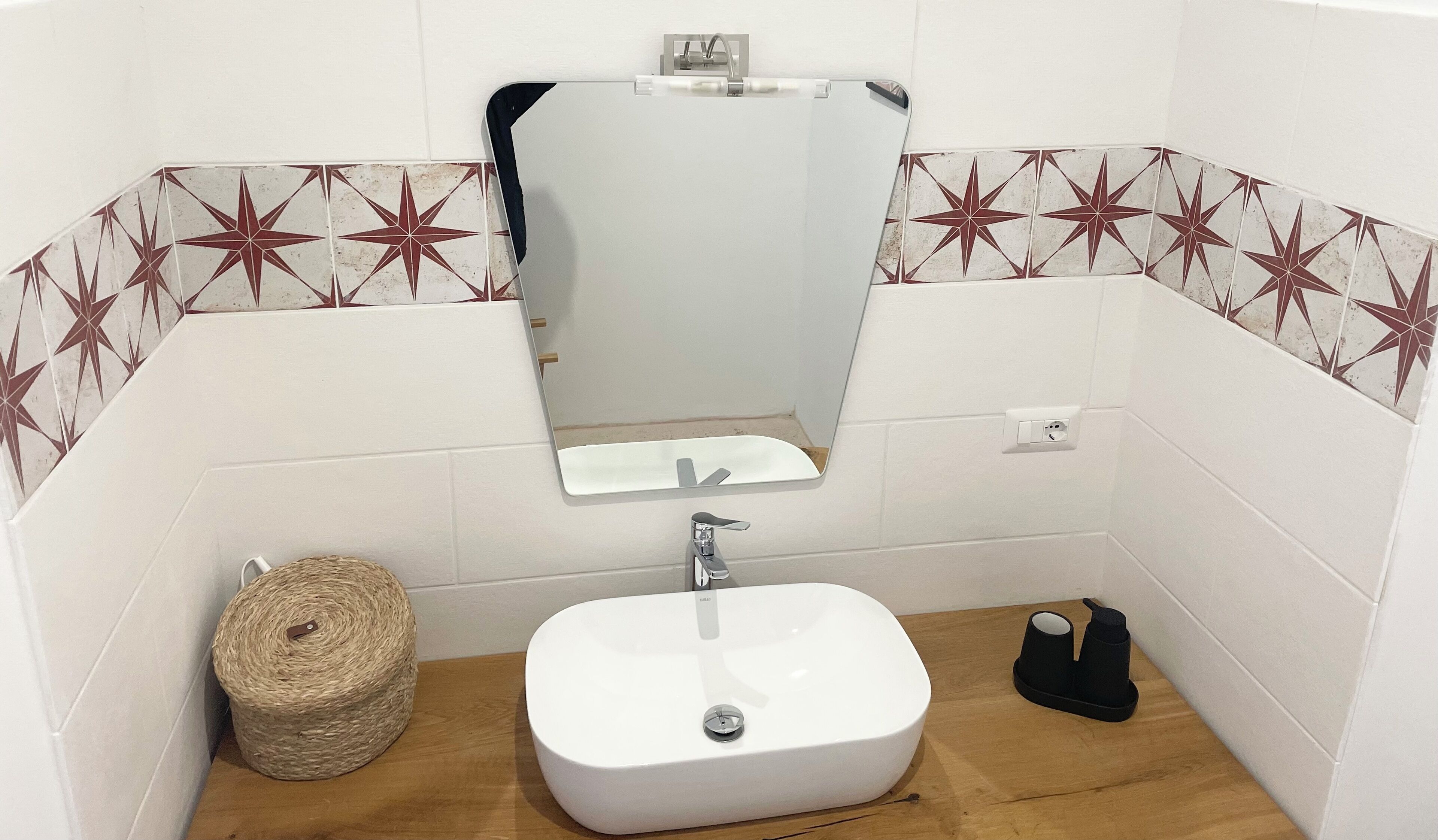 Un baño con un lavamanos blanco, un espejo encima y un salpicadero de azulejos con motivos de estrellas.