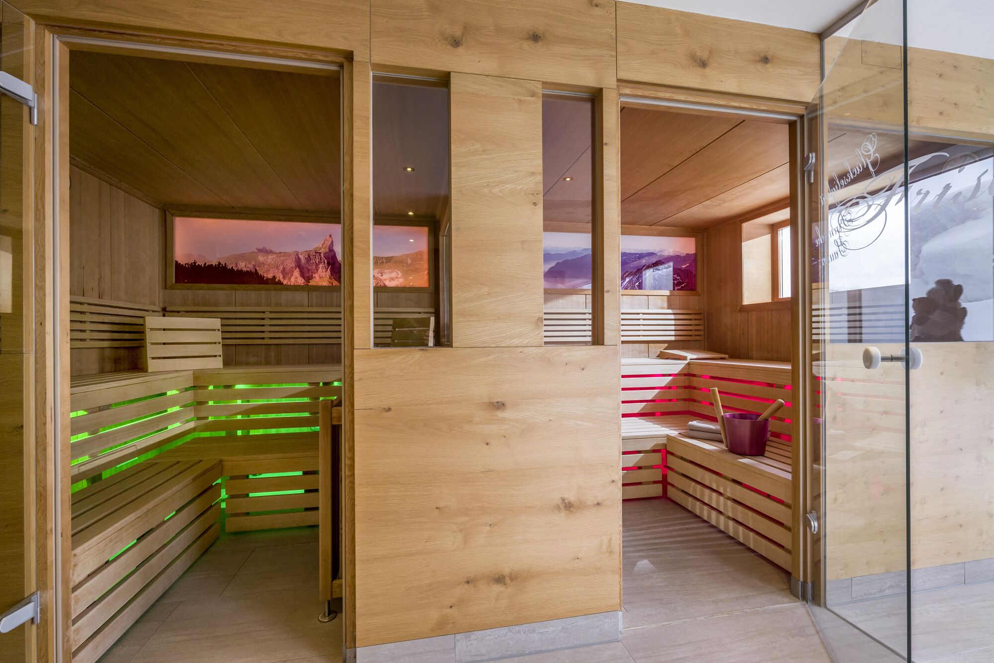 A sauna with wooden benches and glass doors, featuring a mountain view.