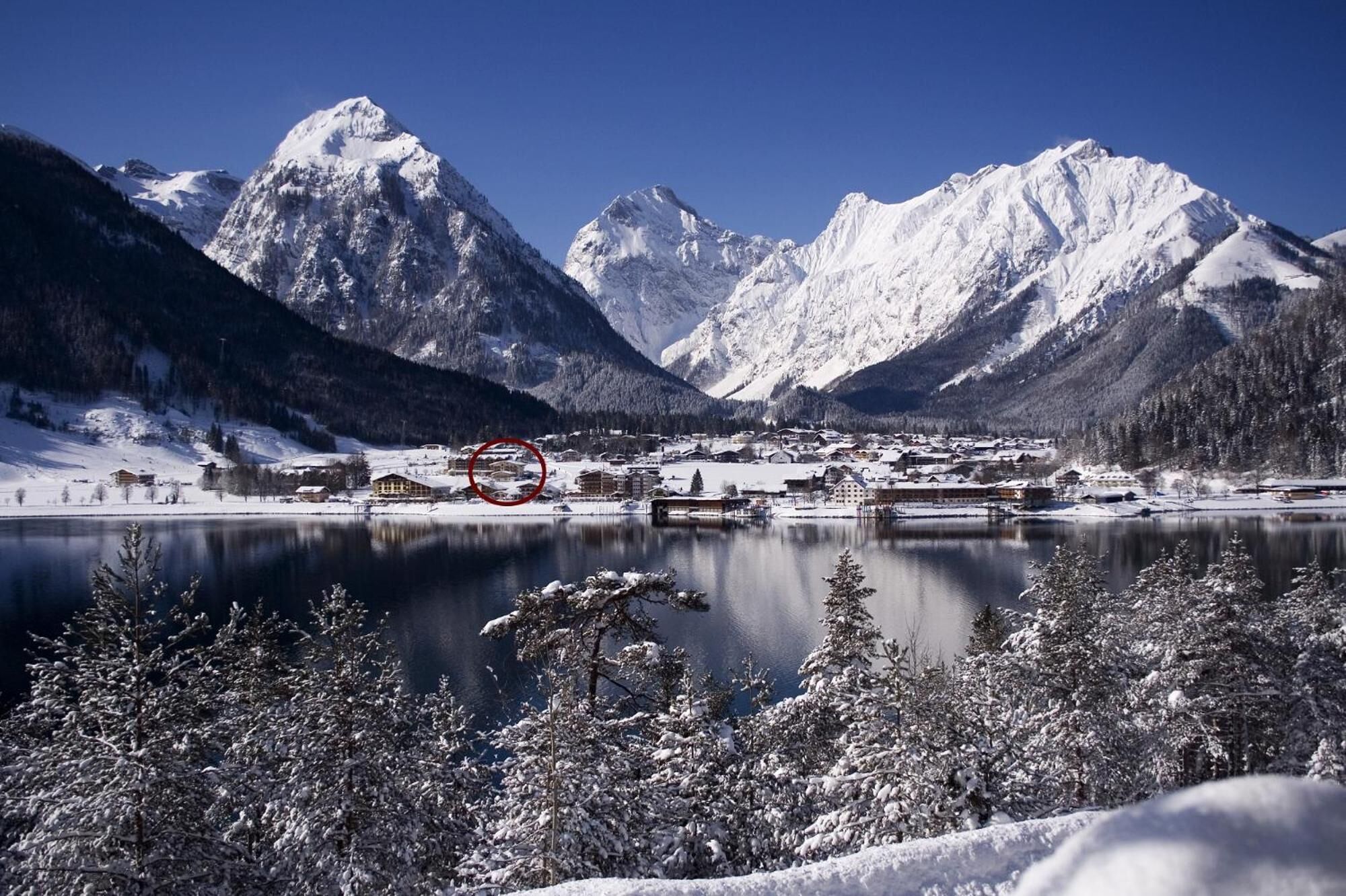 A snow-covered mountain landscape with a lake and buildings in the foreground.