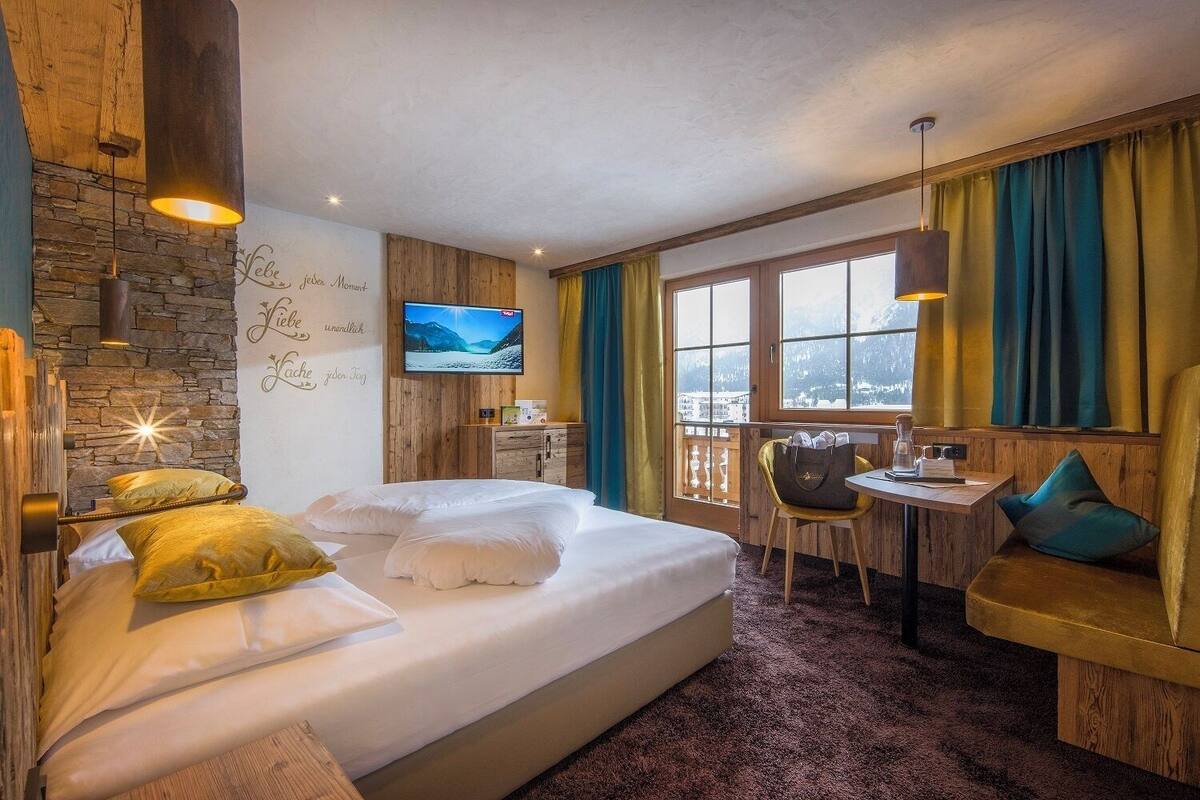A hotel room with a large bed, a desk with a chair, a television, and a view of a snowy landscape through the window.