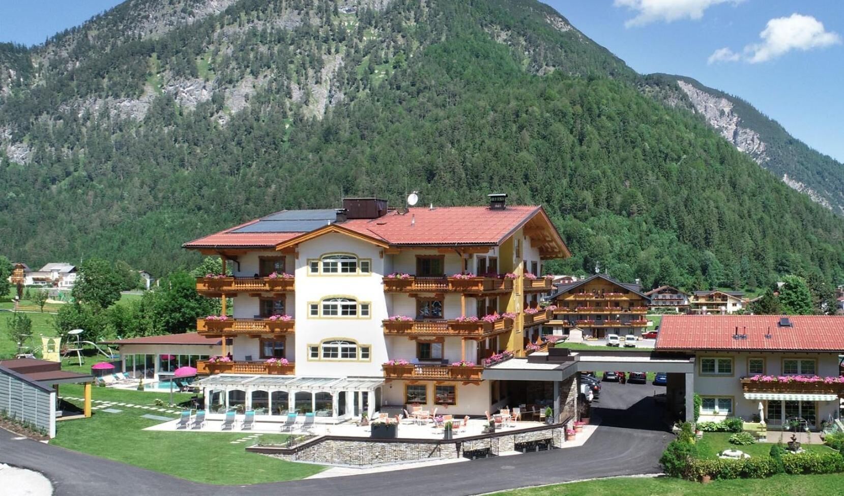 Un hotel de varios pisos con balcones, piscina y montañas al fondo.