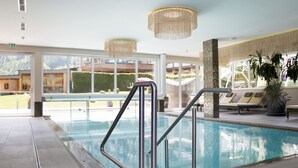 En indendørs swimmingpool med glasvægge, gelændere i metal og udsigt til det fri.