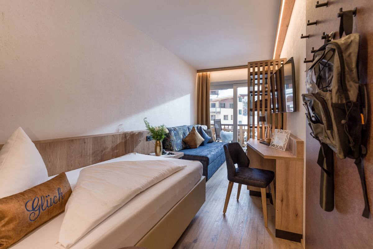 A compact hotel room with a bed, a desk, a chair, and a view of the outside.