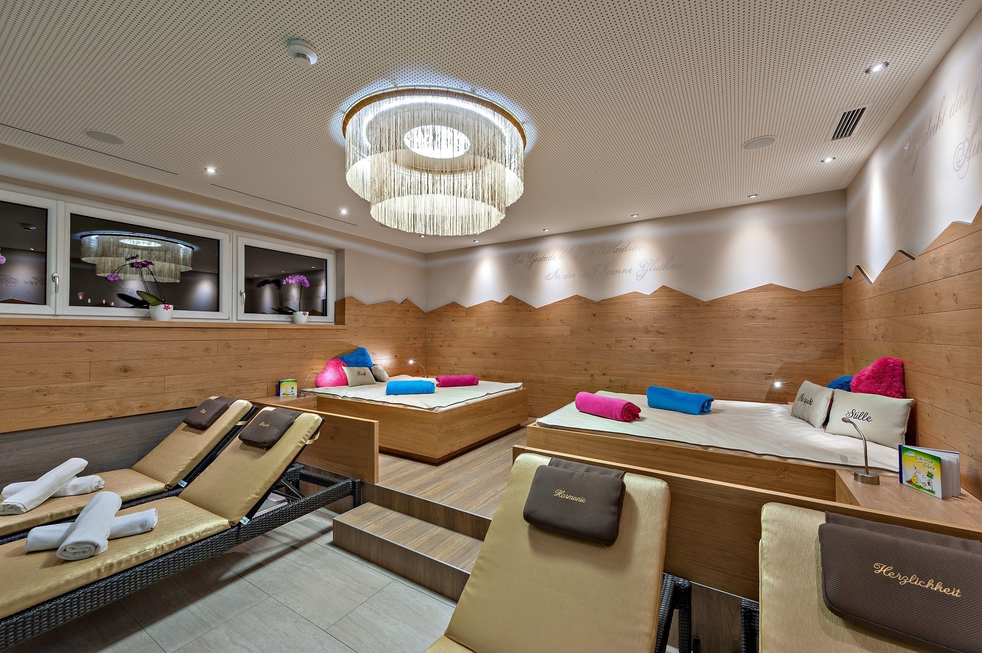 A spa room with two massage tables, wooden panel walls, a ceiling with a perforated design, and a chandelier.