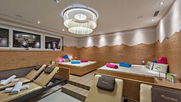 A spa room with two massage tables, wooden panel walls, a ceiling with a perforated design, and a chandelier.