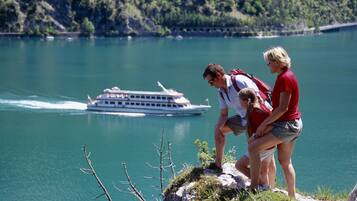 Ein See mit einem Boot in der Ferne, felsiges Gelände und eine Person, die auf einer Klippe steht.