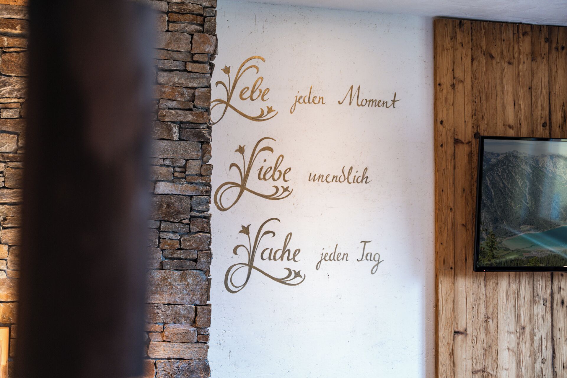 A wall with a decorative phrase in a foreign language, a stone wall on the left, and a wooden panel on the right.