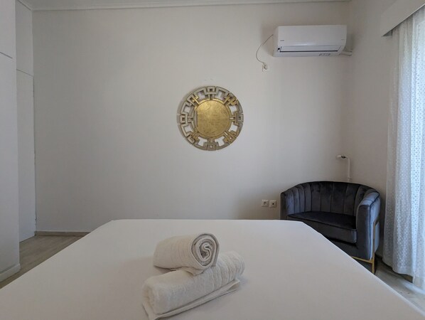 A hotel room with a bed, a decorative wall piece, an air conditioning unit, and a dark-colored armchair.