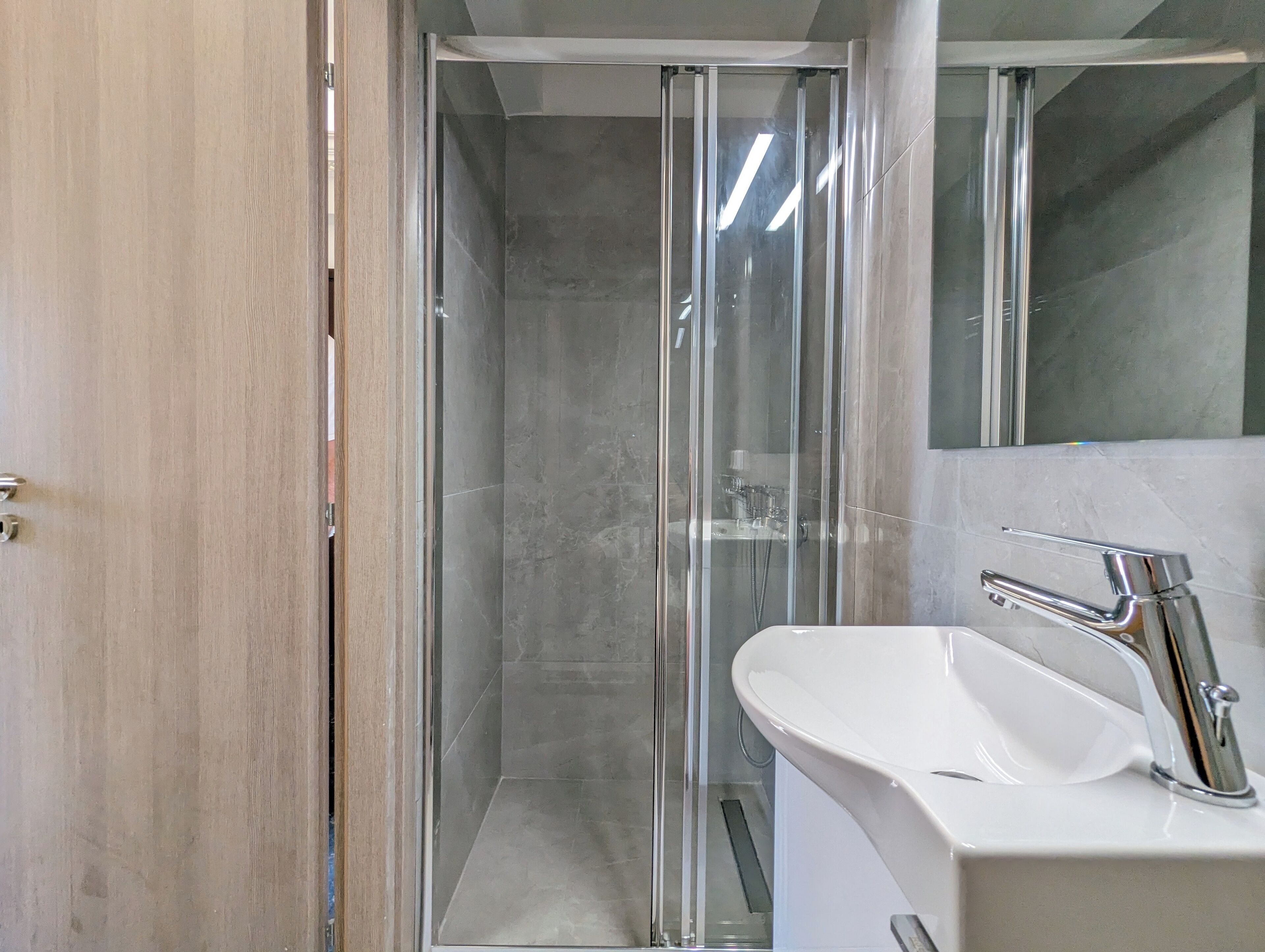 A modern bathroom with a glass-enclosed shower, a white sink, and a mirror above the sink.