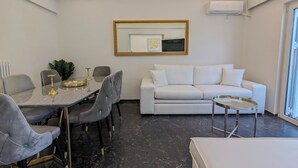 Uma sala de estar moderna com área de jantar, móveis brancos, uma mesa de mármore e um espelho grande na parede.