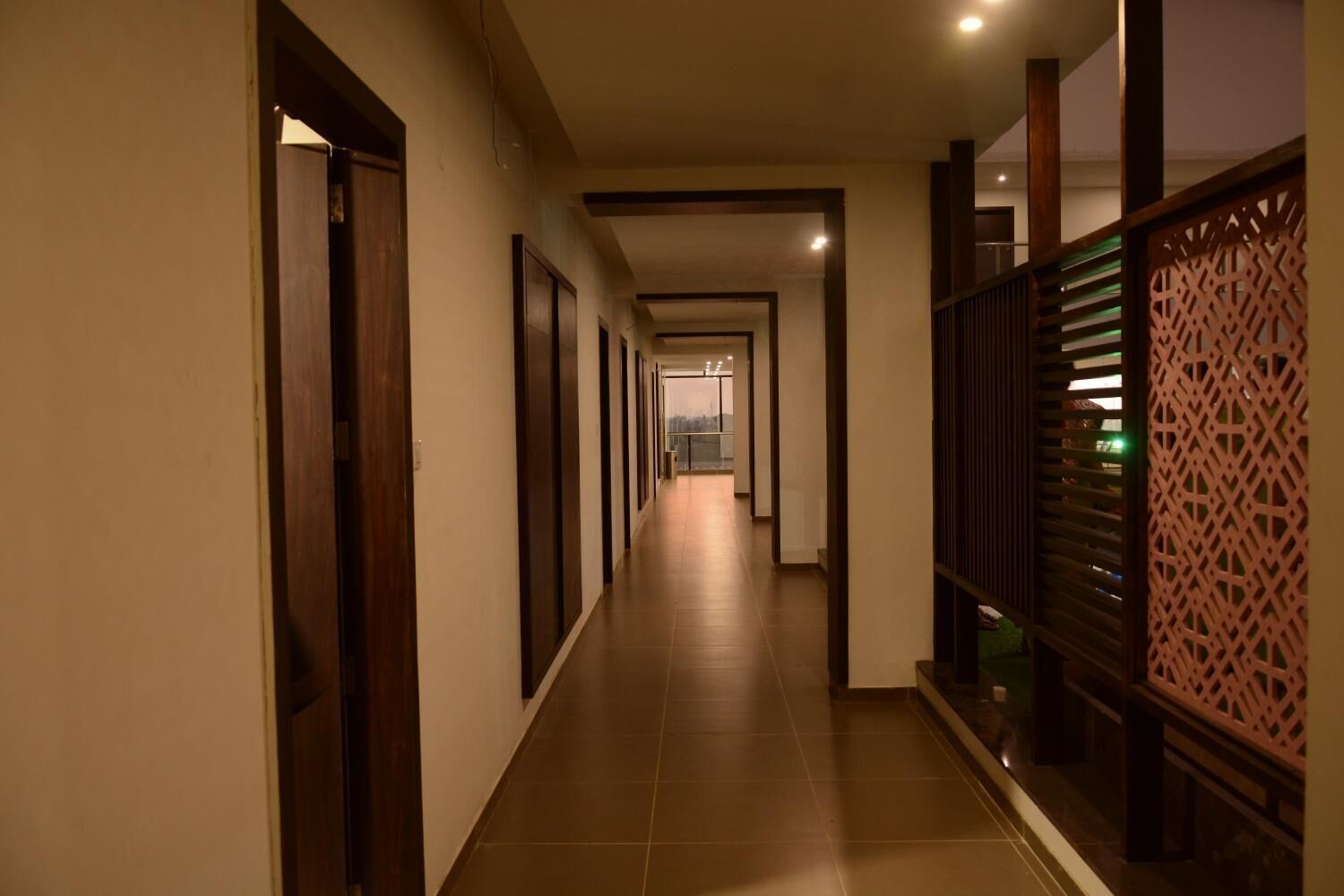 A long, narrow hotel corridor with wooden doors on one side and a decorative partition on the other.