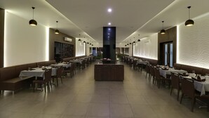 A spacious, modern restaurant with a long counter and multiple tables, featuring a central island and pendant lighting. - The Divine Resort (Veraval)