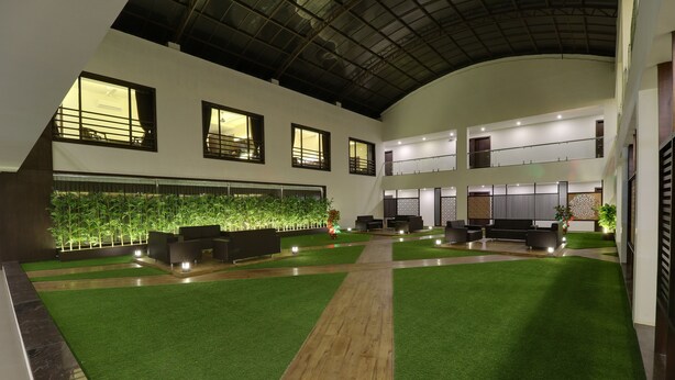 A spacious indoor area with artificial grass, seating arrangements, and a wall with vertical gardens. - The Divine Resort (Veraval)