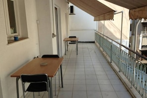 A balcony with a wooden table and chairs, a metal railing, and a tiled floor.
