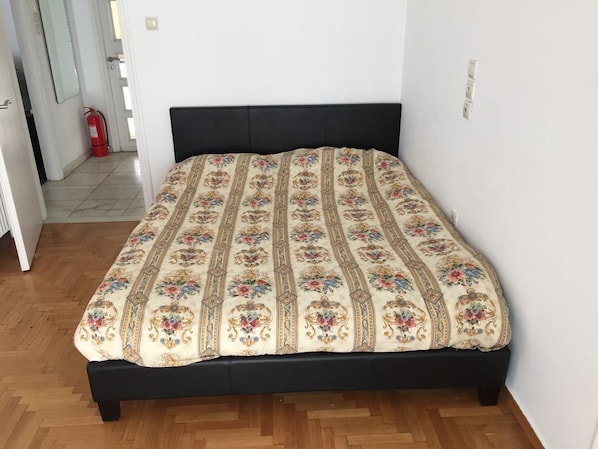 A bed with a floral-patterned bedspread, a black headboard, and a wooden floor.