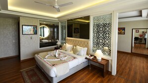 A modern hotel room with a large bed, a ceiling fan, a bedside table with a lamp, and a decorative mirror. - Stardom Resort (Jaipur)