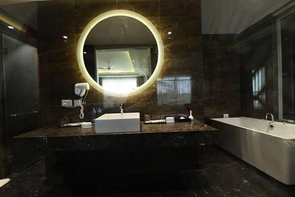 Une salle de bain moderne avec un grand miroir ovale, un lavabo sur pied et une baignoire îlot.