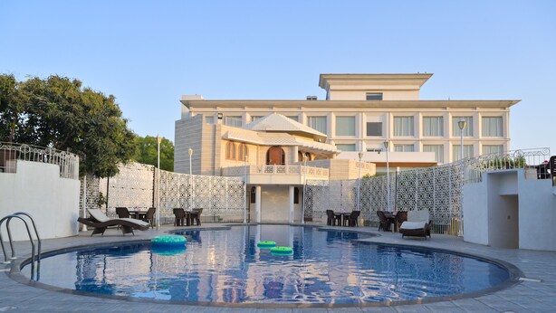 A swimming pool with lounge chairs and a building in the background. - Stardom Resort (Jaipur)