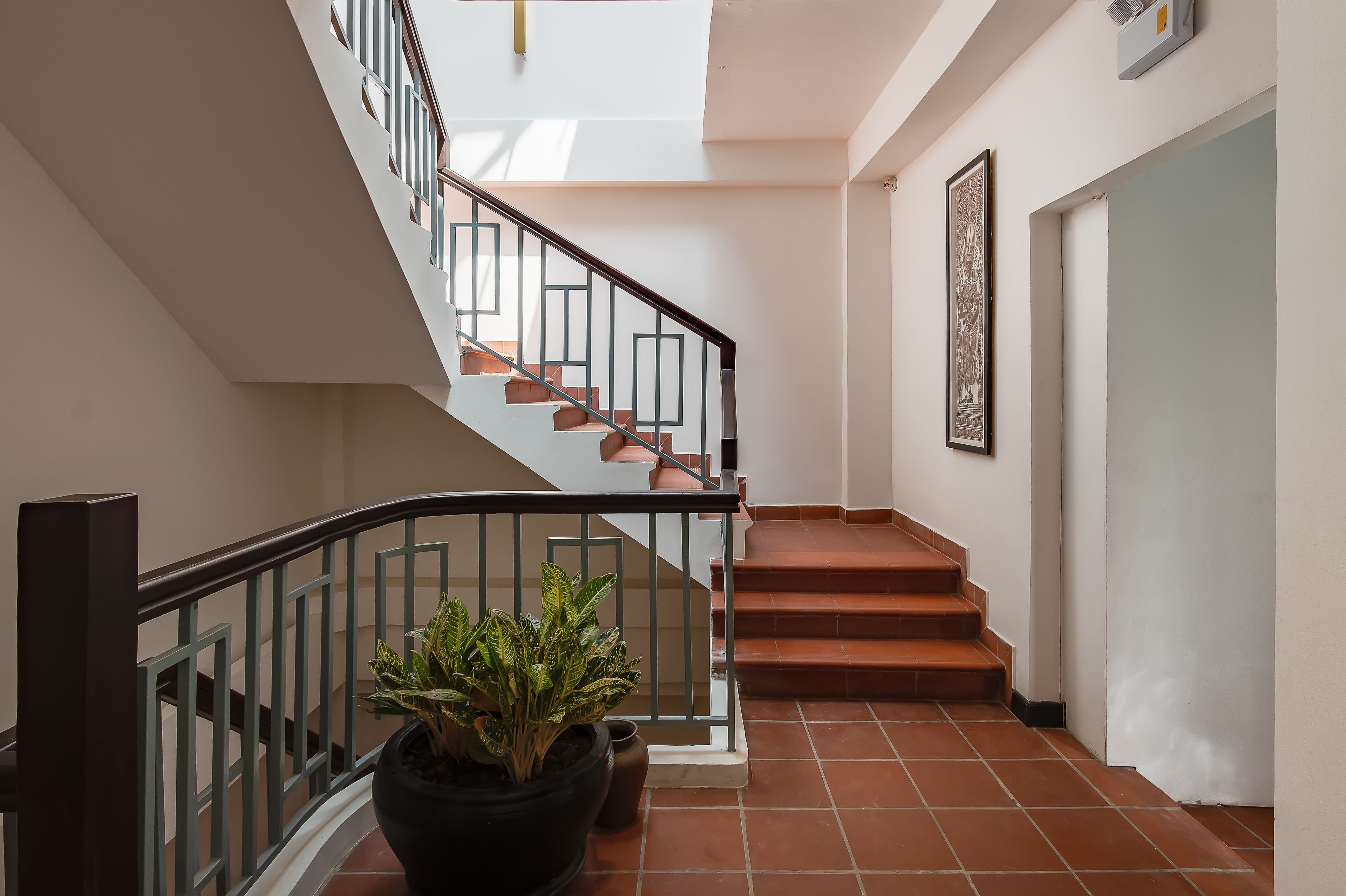 Una escalera con barandilla de metal, una planta en maceta y un cuadro en la pared.