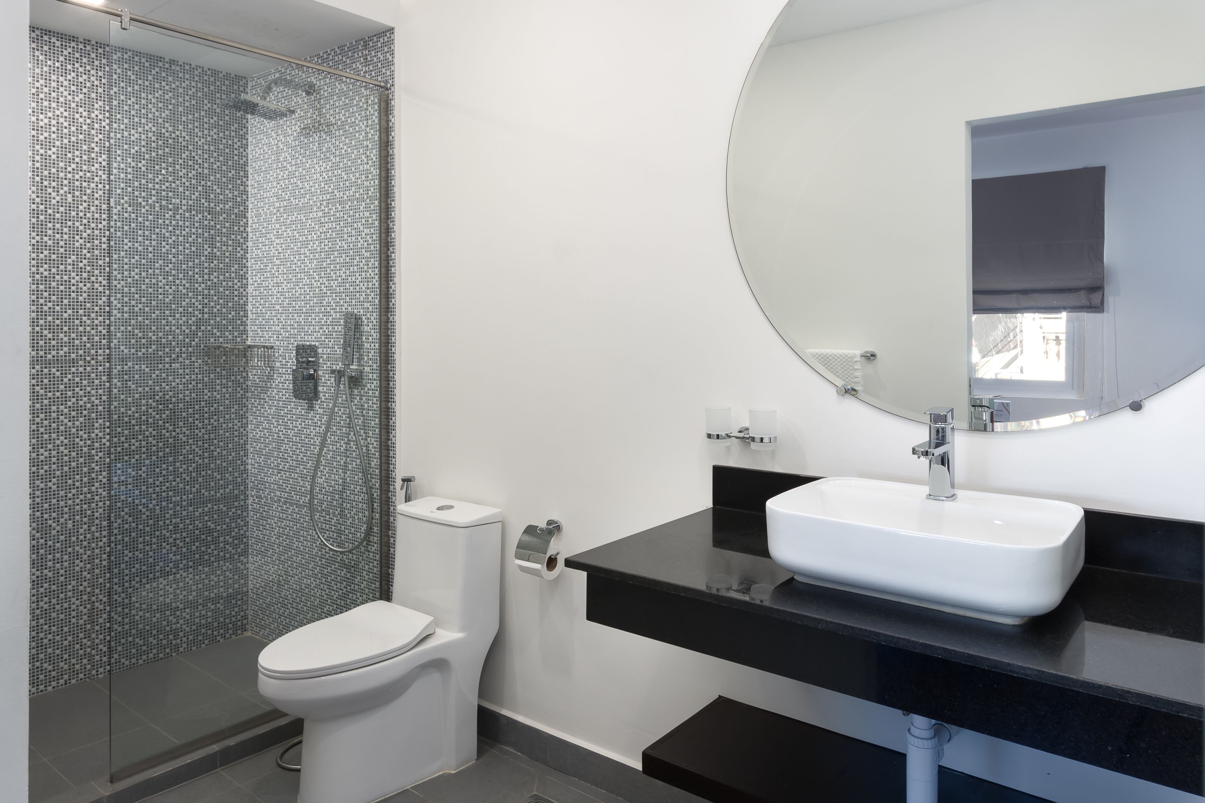 Une salle de bain moderne avec une douche en verre, des toilettes blanches et un comptoir noir agrémenté d’un lavabo et d’un miroir blancs.