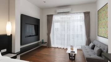 A modern hotel room with a flat-screen TV, a sofa, a small table, and a large window with sheer curtains.