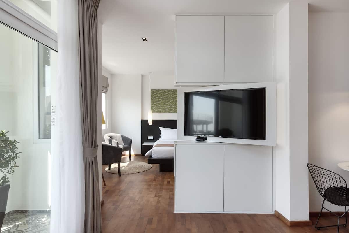Moderni hotellihuone, jossa on suuri televisio, joka on kiinnitetty valkoiseen kaappiin, valkoisilla lakanoiden peitetty sänky, pieni työpöytä ja tuoli.