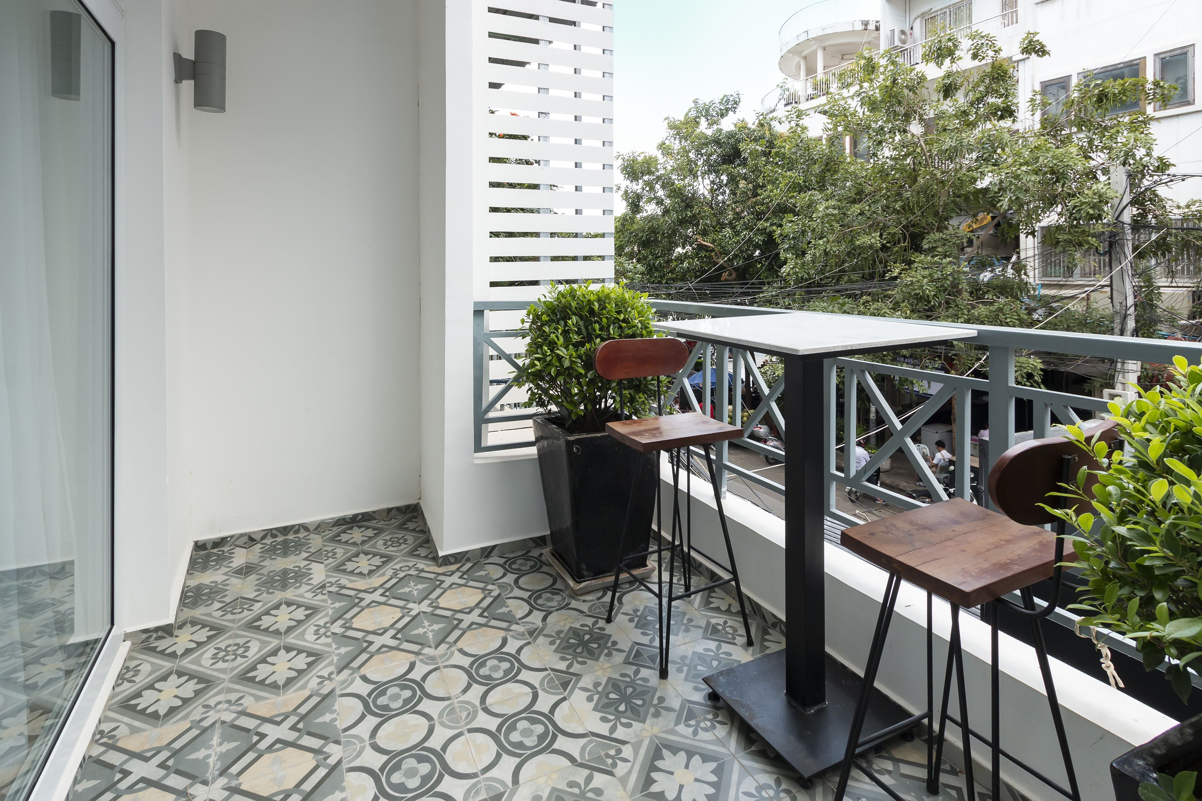 Ein Balkon mit gemusterten Fliesen, einem Blumentopf, einem Holztisch und einem Stuhl.