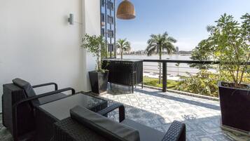 Ein Balkon mit Tisch und Stühlen, einer hängenden Leuchte, Topfpflanzen und Blick auf einen Fluss und Palmen.