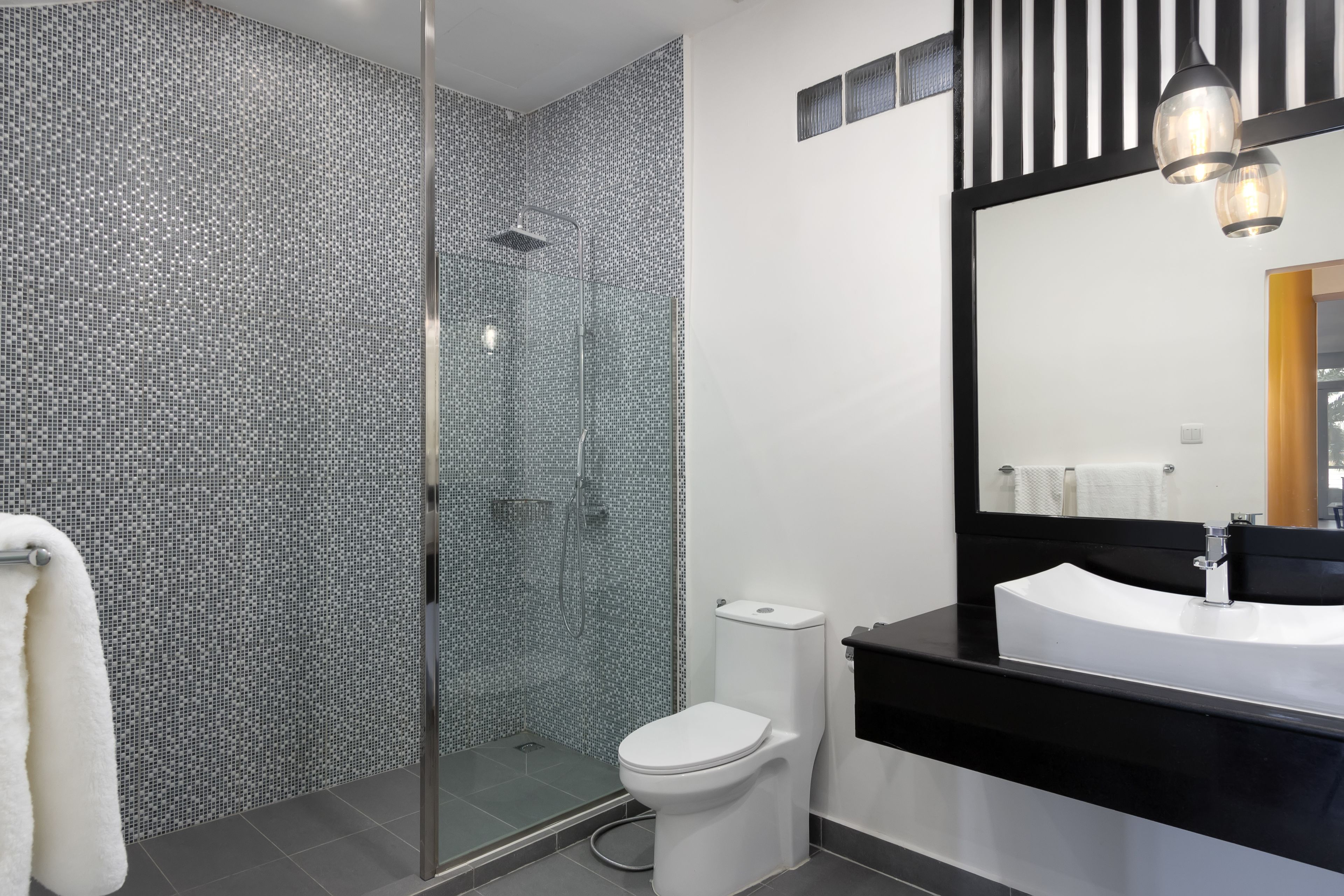 Un bagno moderno con doccia vetrata, un water bianco e un mobile lavabo nero con uno specchio grande.