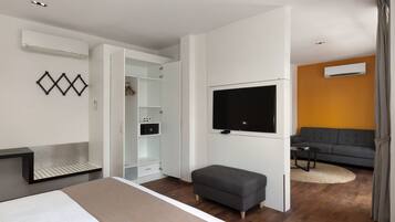 A modern hotel room with a bed, a grey sofa, a TV mounted on the wall, and a wardrobe with a mirror.