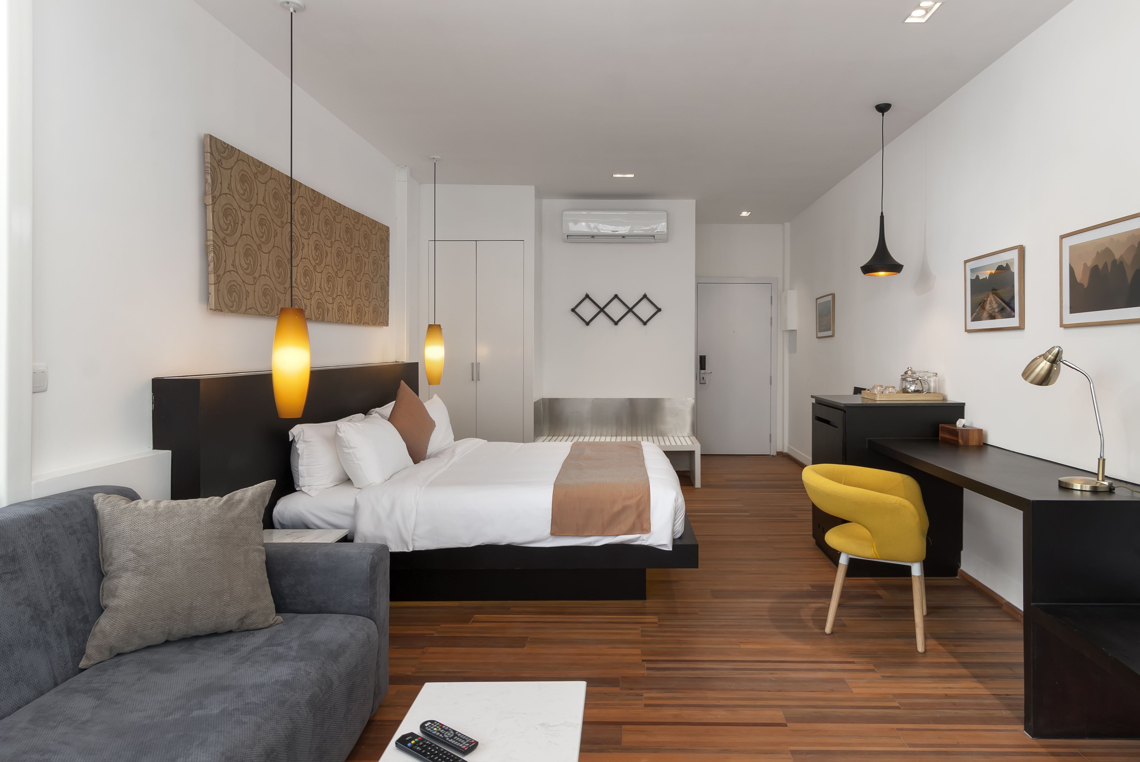 A modern hotel room with a bed, a desk, a sofa, and a chair.