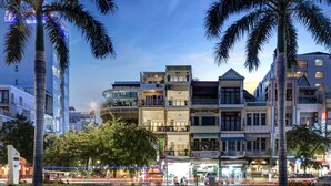 A multi-story building with balconies and large windows, surrounded by palm trees and a busy street with vehicles. - Tao Riverside Residence (Phnom Penh)