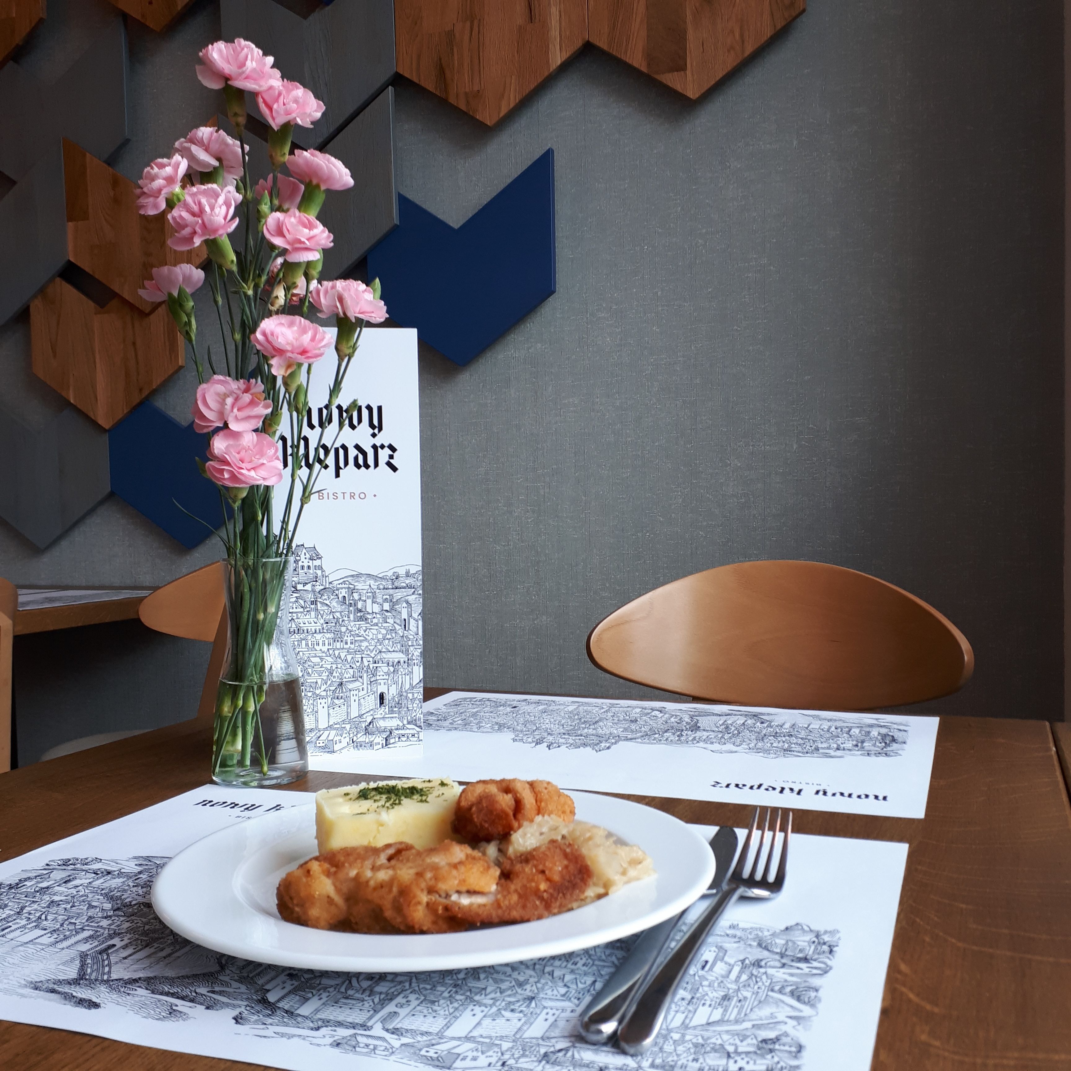 A table with a plate of food, a vase of flowers, and a menu.
