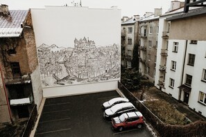 A parking area with three cars, a mural of a cityscape on the wall, and adjacent residential buildings. - Avena Boutique Hotel by Artery Hotels (Kraków)