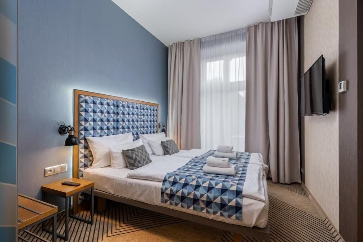 A hotel room with a bed, a desk, a chair, a television, and a window with curtains.