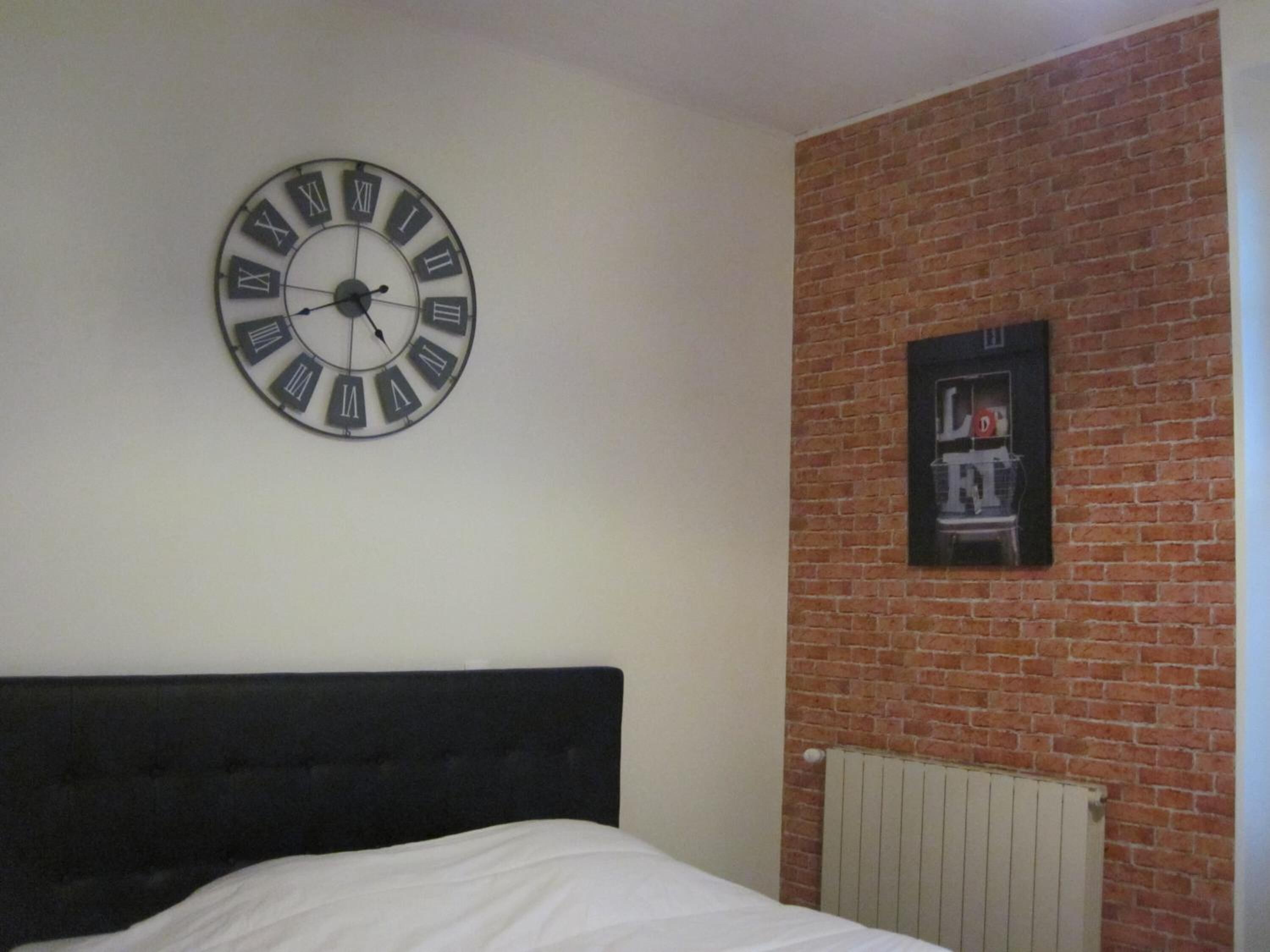 A bedroom with a black headboard, a round wall clock, and a brick wall.