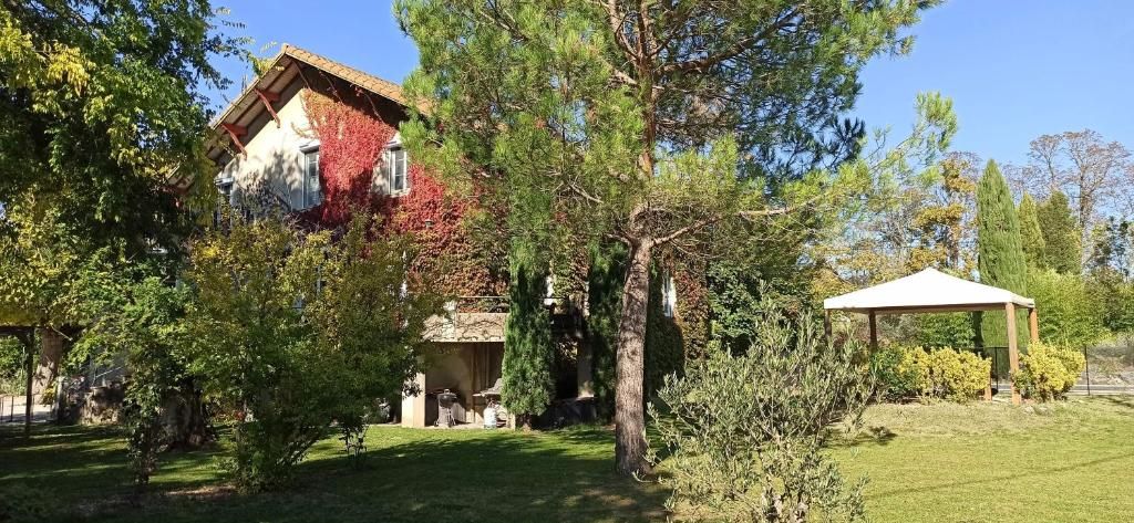 Uma casa com jardim, um gazebo e uma árvore com folhas vermelhas.