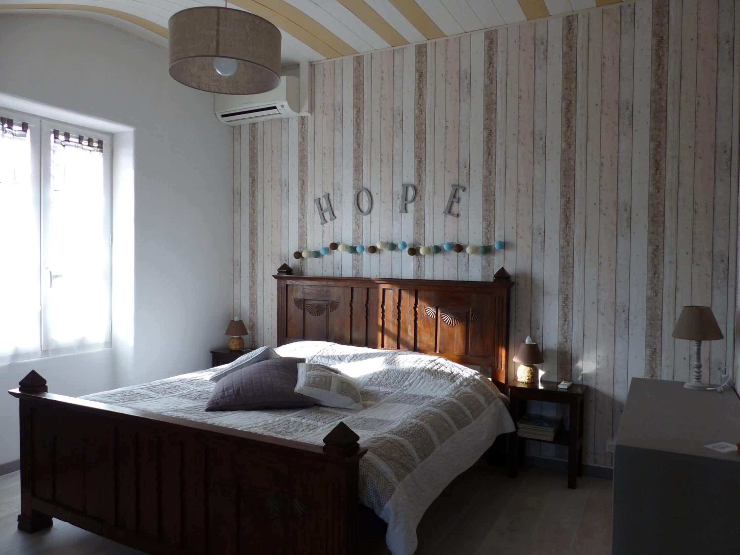 Un dormitorio con una cama de madera, un aire acondicionado instalado en la pared, un letrero decorativo que dice "HOPE" y una lámpara en una mesita de noche.