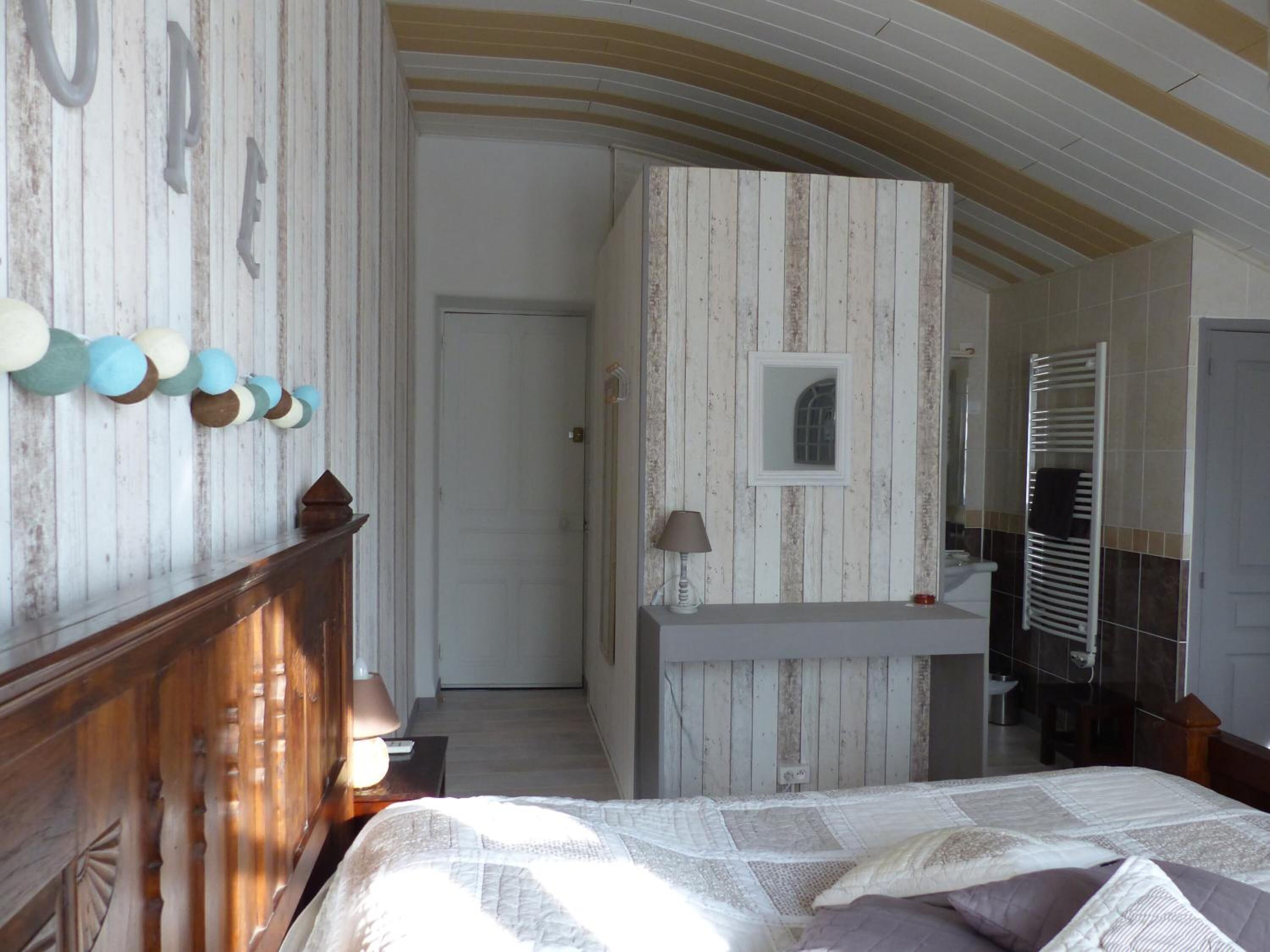 A bedroom with a wooden headboard, a bed with a quilt, a bedside table with a lamp, and a mirror above the bed.