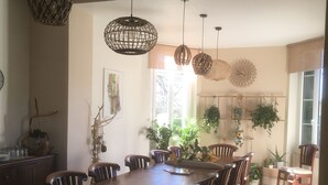 Un comedor con una larga mesa de madera, varias sillas, lámparas colgantes de fibras naturales y plantas en macetas.