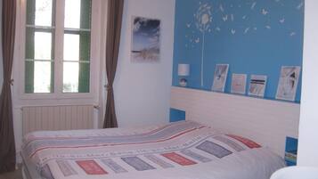 A bedroom with a bed, a window with curtains, a wall with framed pictures, and a blue accent wall.