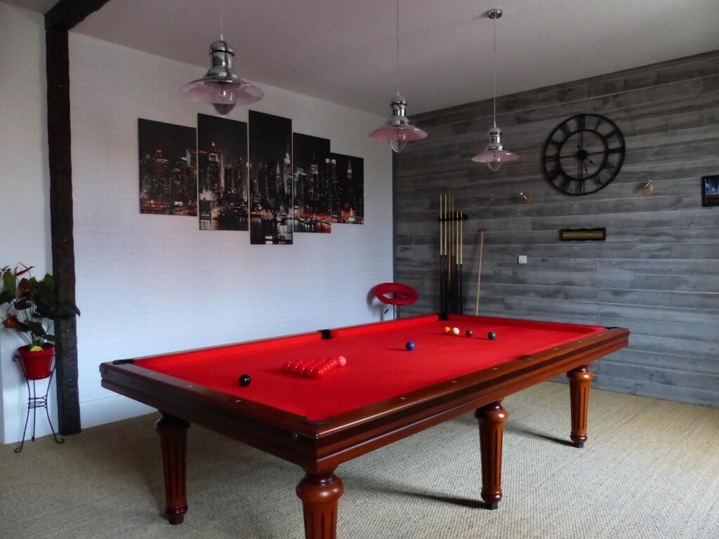 A pool table with a red felt surface, a clock, and cityscape artwork on the wall.