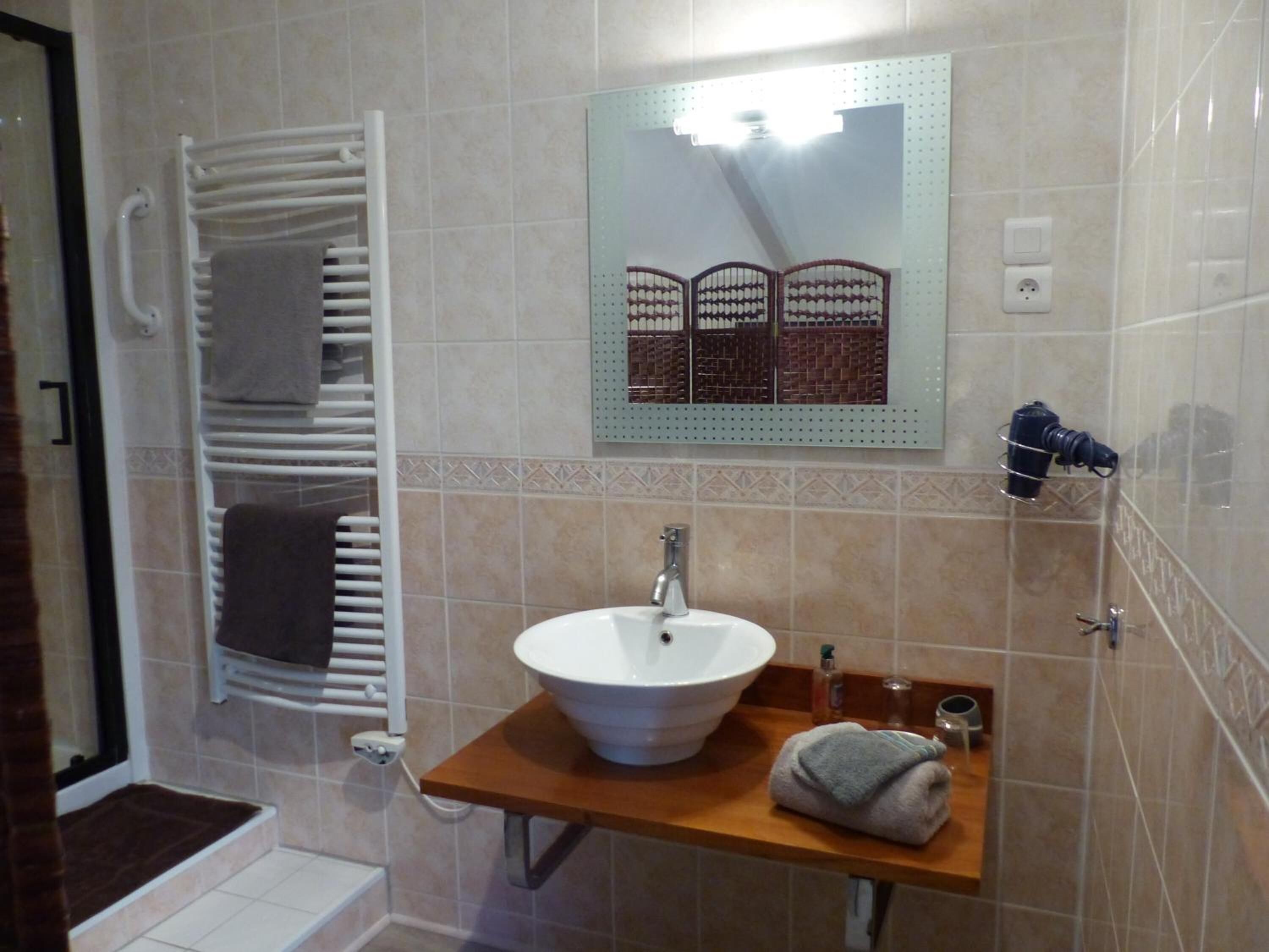 Ein Badezimmer mit weißem Waschbecken, einem Handtuchhalter, einem Spiegel mit Zierrahmen und einer Duschkabine.